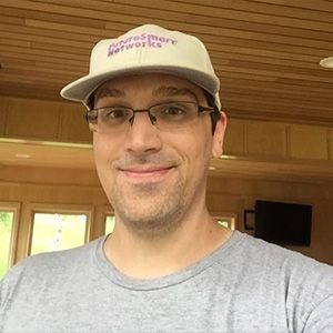 headshot of man wearing glasses and hat